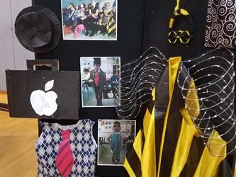 Student art panel depicting two design projects. One design project is a black hat, a black briefcase with the Apple logo and a blue and white pattern vest with a red and blue striped tie. The other is a bumblebee costume with wires for wings and an eye mask.